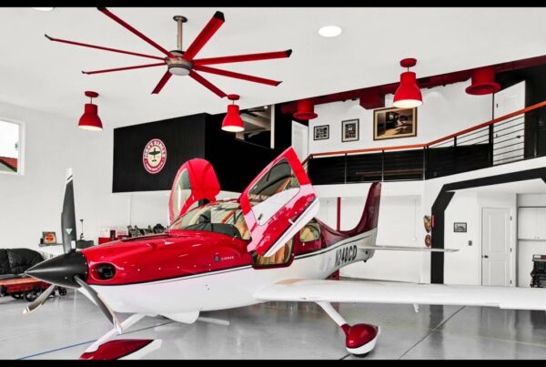 interior of hangar home shows red prop airplane parked in garage with matching red overhead spotlights and large ceiling fan