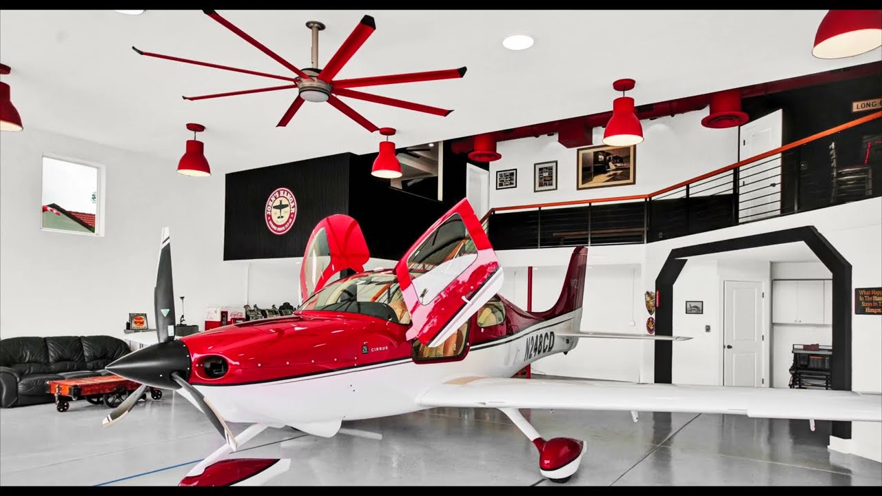 interior of hangar home shows red prop airplane parked in garage with matching red overhead spotlights and large ceiling fan