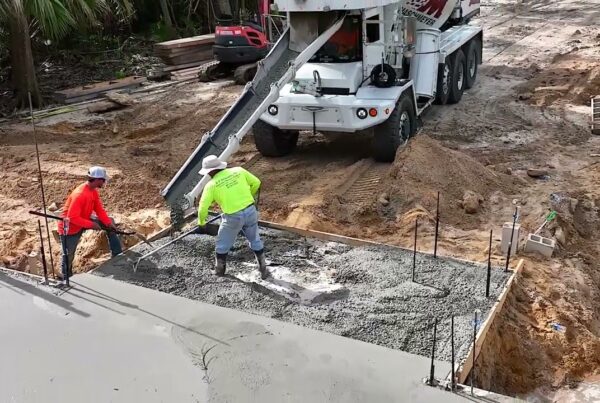 two workers pour wet cement into a section of the foundation for a residential home