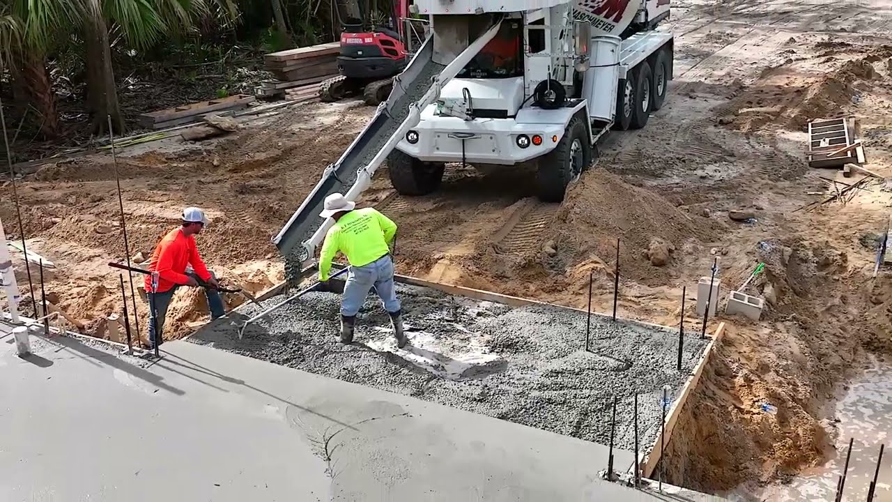 two workers pour wet cement into a section of the foundation for a residential home