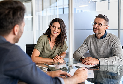 a young couple sits with an employee at a conference table in an office setting