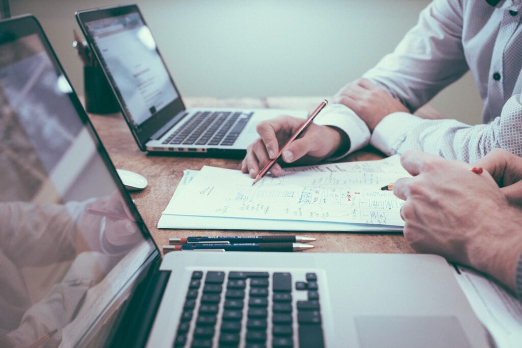 business meeting with laptops side by side on table while two people review notes